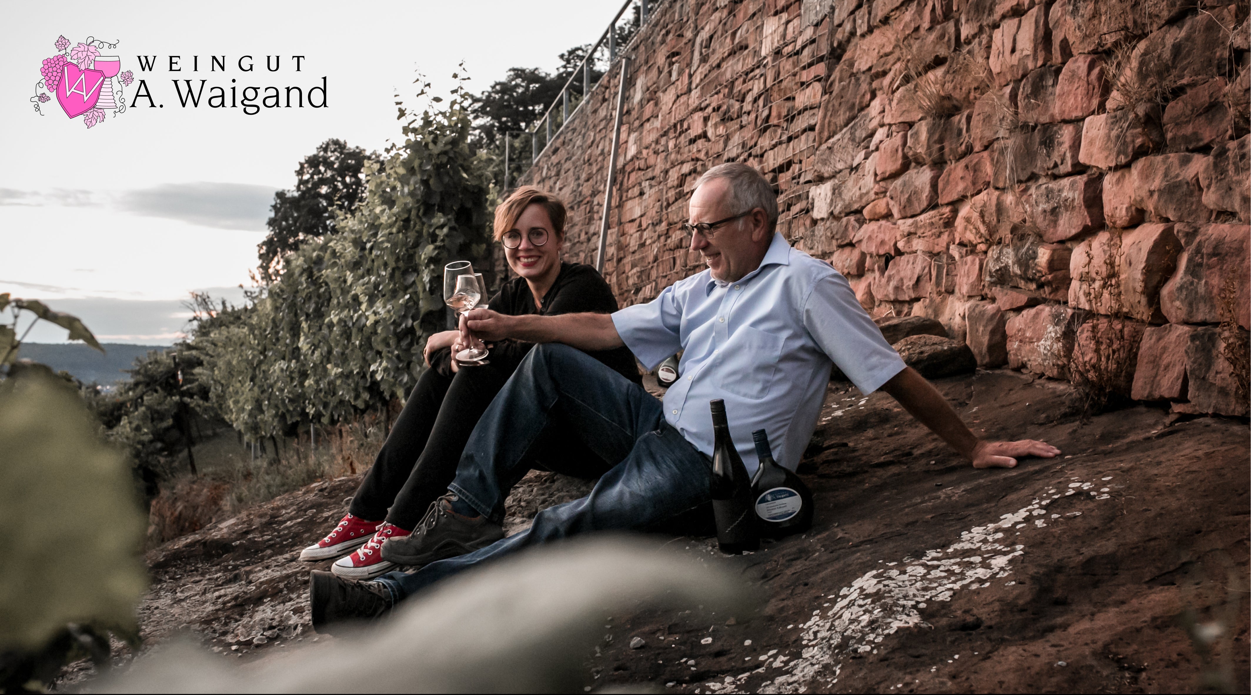 Zwei Personen entspannt an einer Weinbergmauer sitzend – Headerbild Weingut A. Waigand